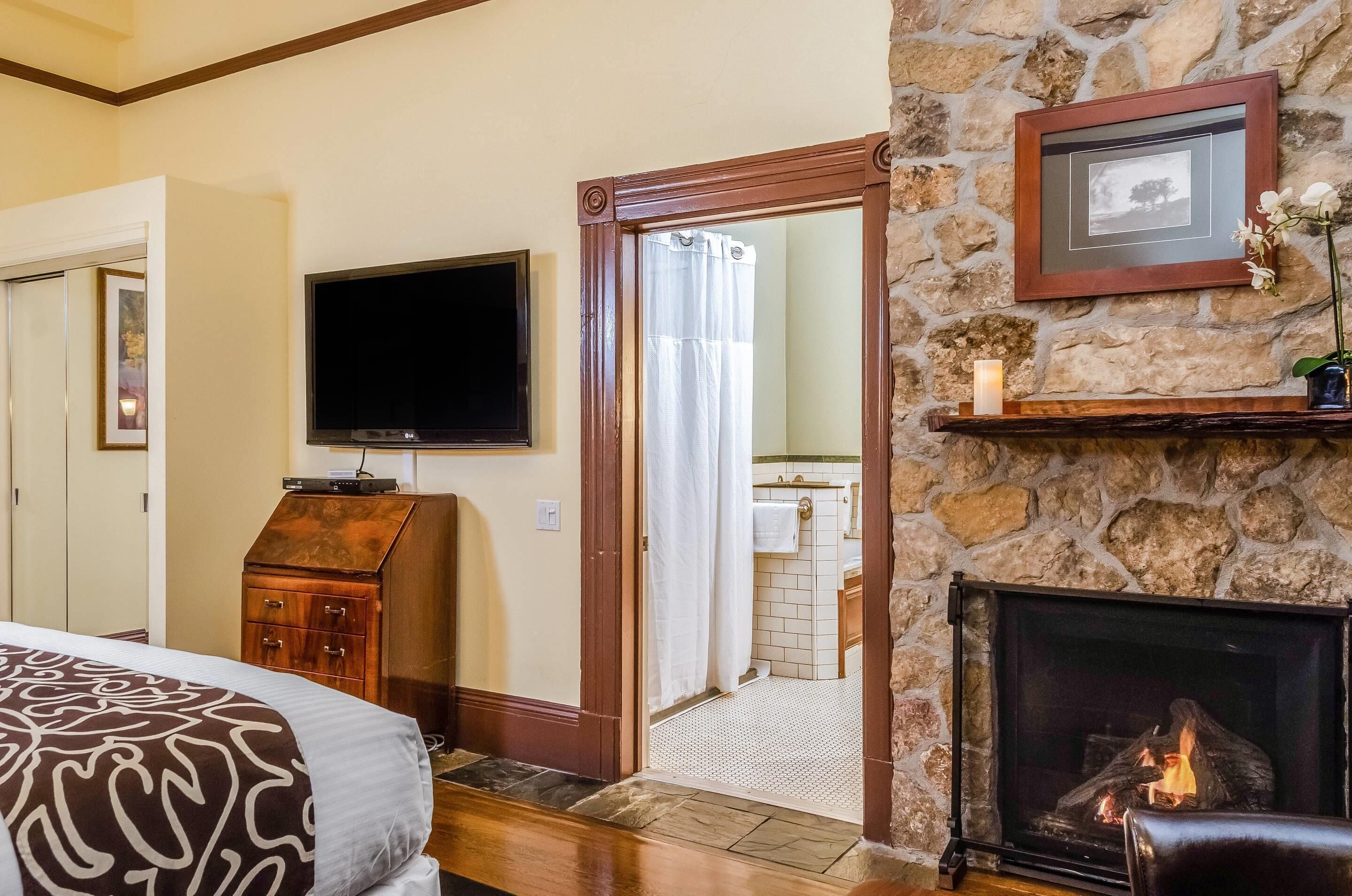 A bedroom with a bed, a television, a fireplace, and a stone wall.