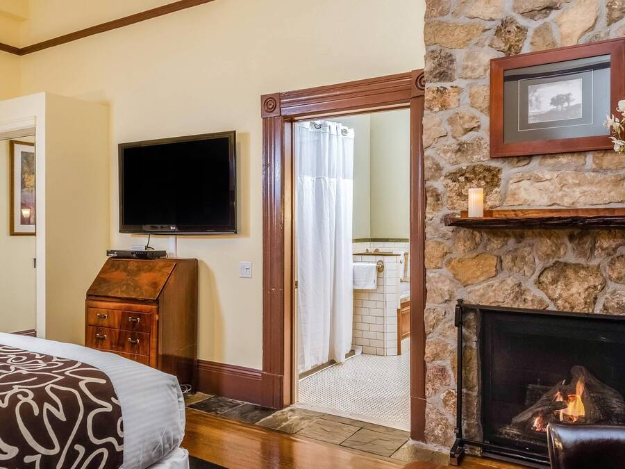 A bedroom with a bed, a television, a fireplace, and a stone wall.