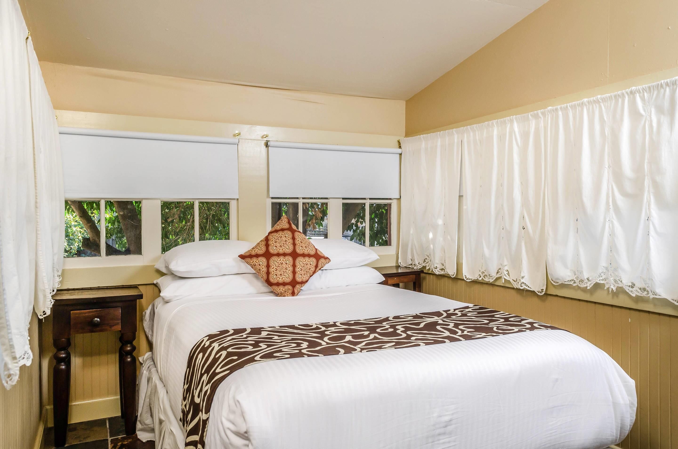 Una cama bien hecha con un edredón estampado, un cojín decorativo y una ventana con cortinas.