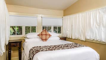 Una cama bien hecha con un edredón estampado, un cojín decorativo y una ventana con cortinas.