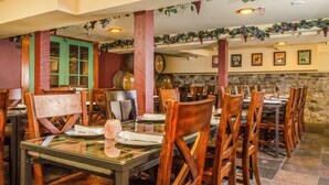A restaurant with wooden chairs and tables, a green door, and wine barrels in the background. - Hotel Napa Valley, an Ascend Collection Hotel (Napa)