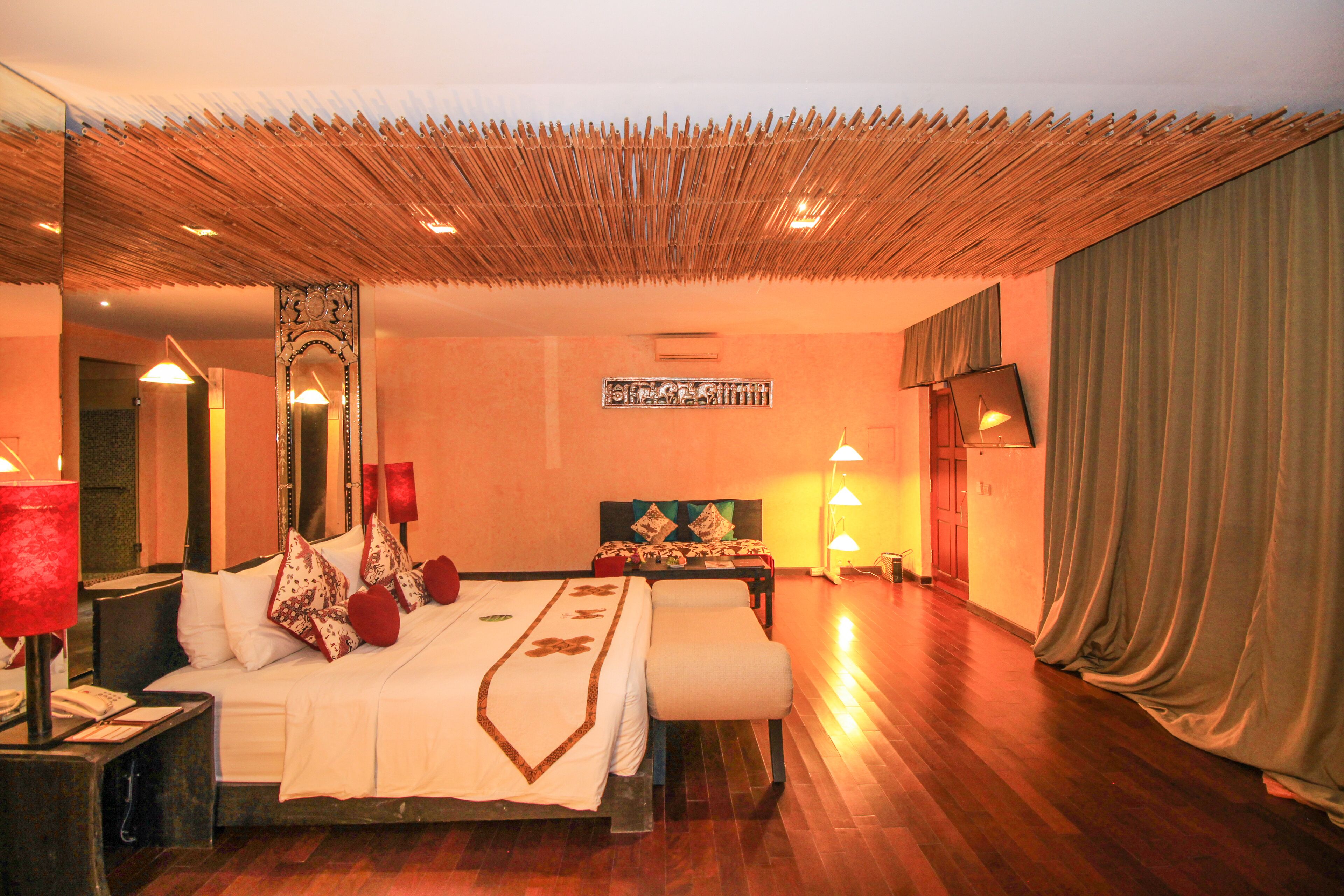 A hotel room with a large bed, bedside tables, a mirror, a headboard, and a curtain.