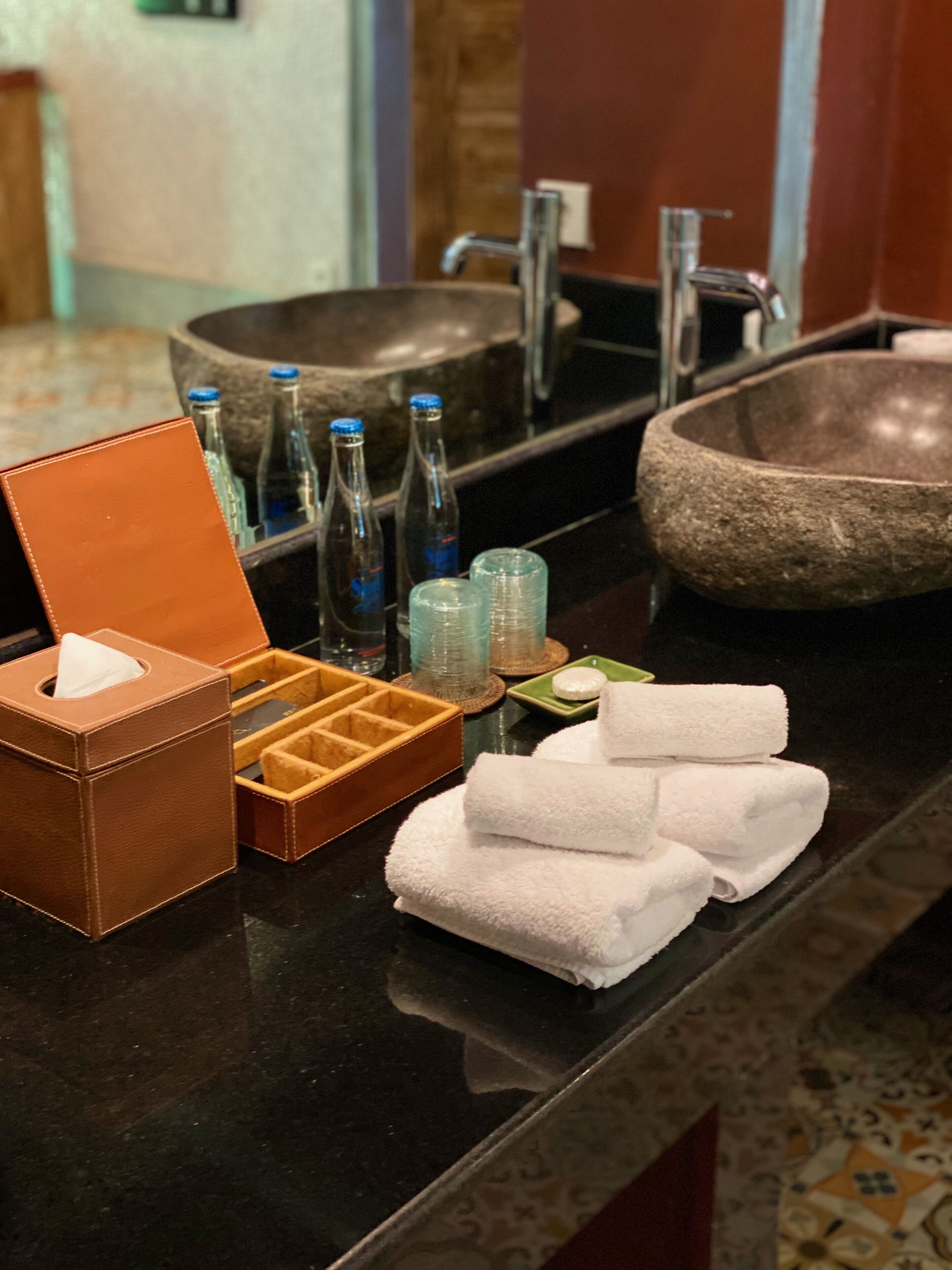 A bathroom counter with a stone sink, bottles, a tissue box, and towels.