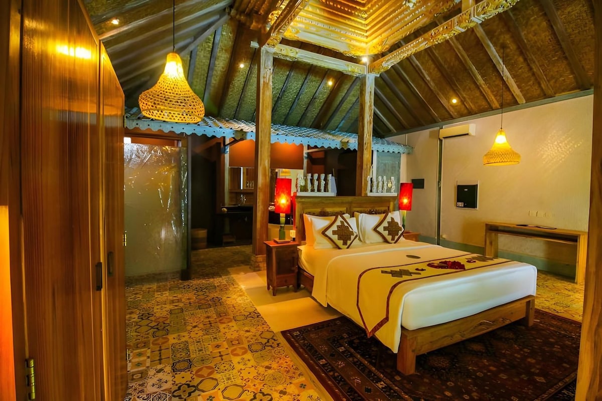 A bedroom with a large bed, a wooden ceiling, and a patterned floor.