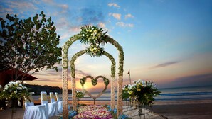 Decoración para una boda en la playa con un arco en forma de corazón, arreglos florales blancos y una mesa con manteles blancos.