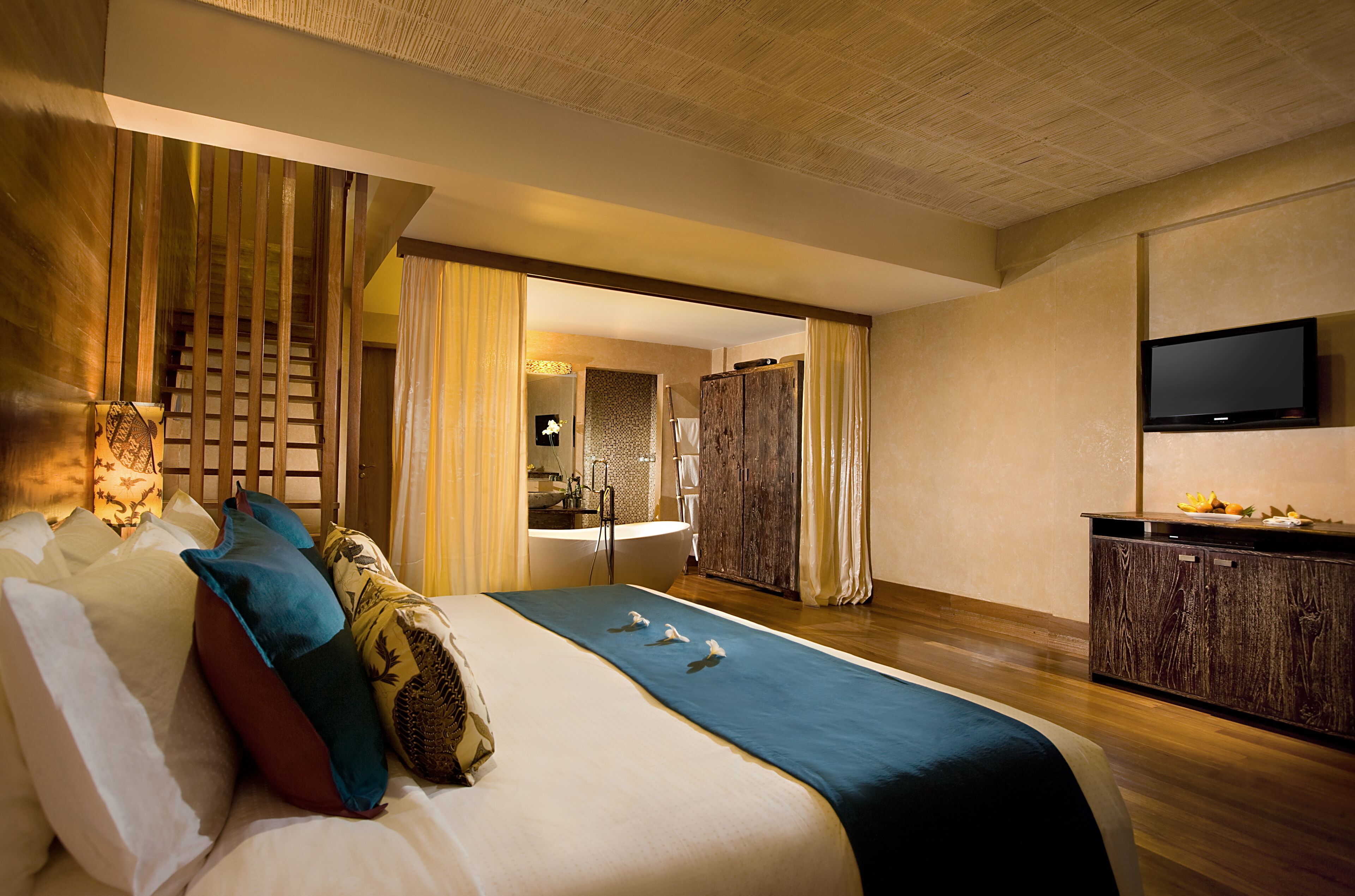 A hotel room with a large bed, a wooden headboard, a television, and a bathroom visible through an open door.
