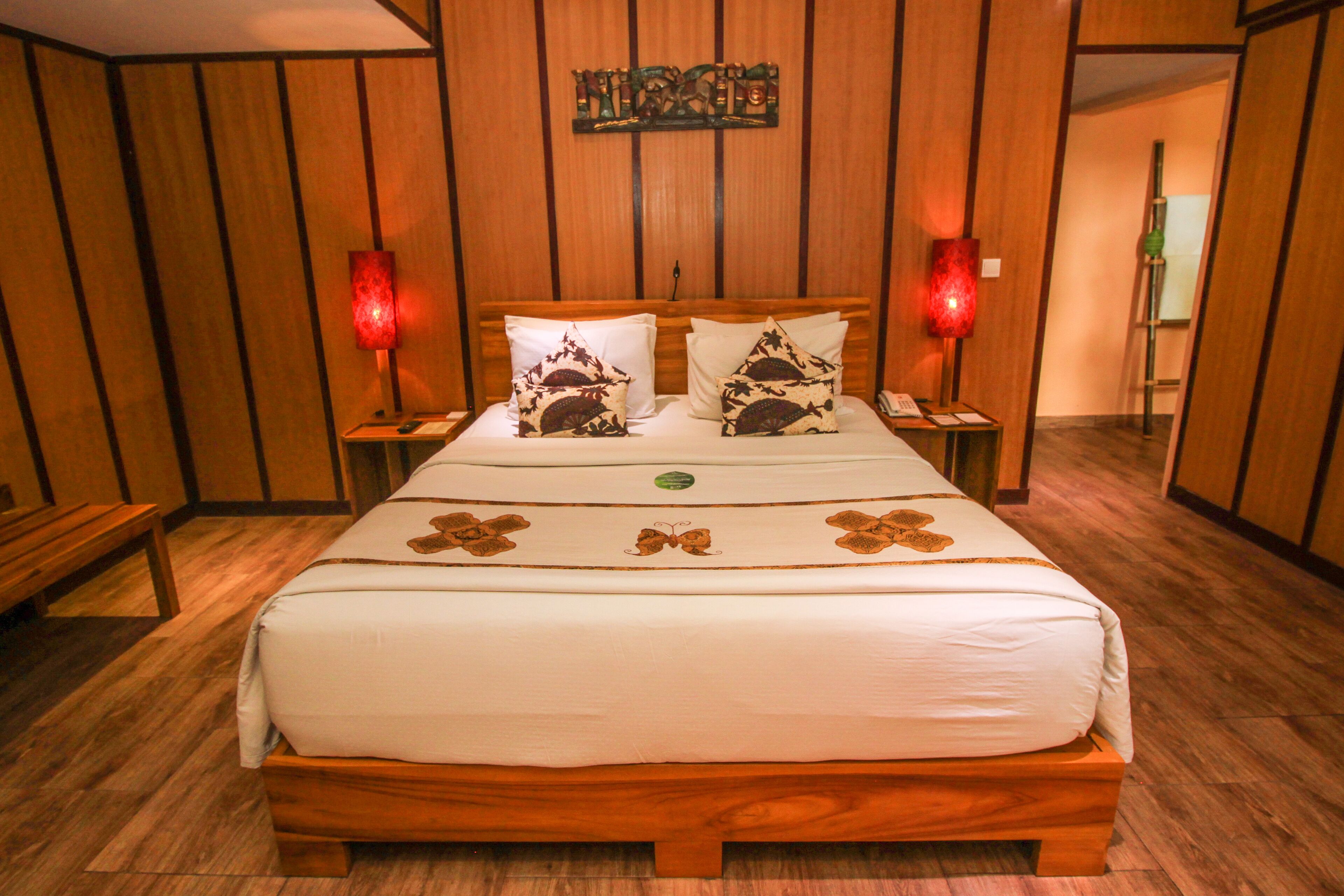 A wooden-paneled room with a bed, two bedside lamps, and a wall-mounted artwork.