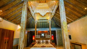 Un lit à baldaquin à quatre poteaux, doté d’une structure en bois et de sculptures complexes, ainsi qu’un banc et une table de chevet avec une lampe.