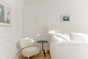 A hotel room with a bed, a chair, a small table, and two framed pictures on the walls. - Coral Sands Motel - In Los Angeles (Hollywood) (Los Angeles)