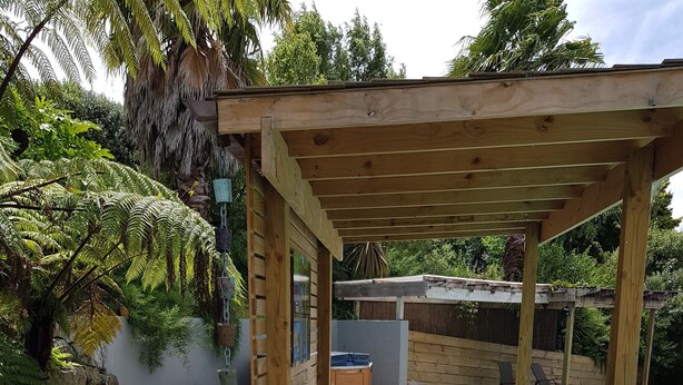 Eine Holzterrasse mit einer Pergola, einem blauen Liegestuhl und einem Pool.