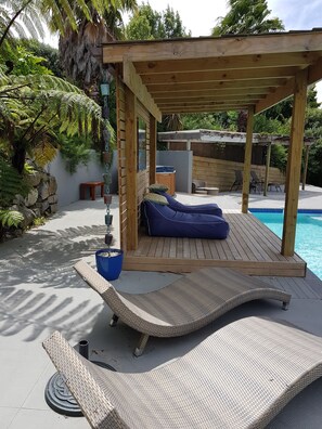 A wooden deck with a pergola, a blue lounge chair, and a pool. - Huntington Stables Retreat Accommodation (Cambridge)
