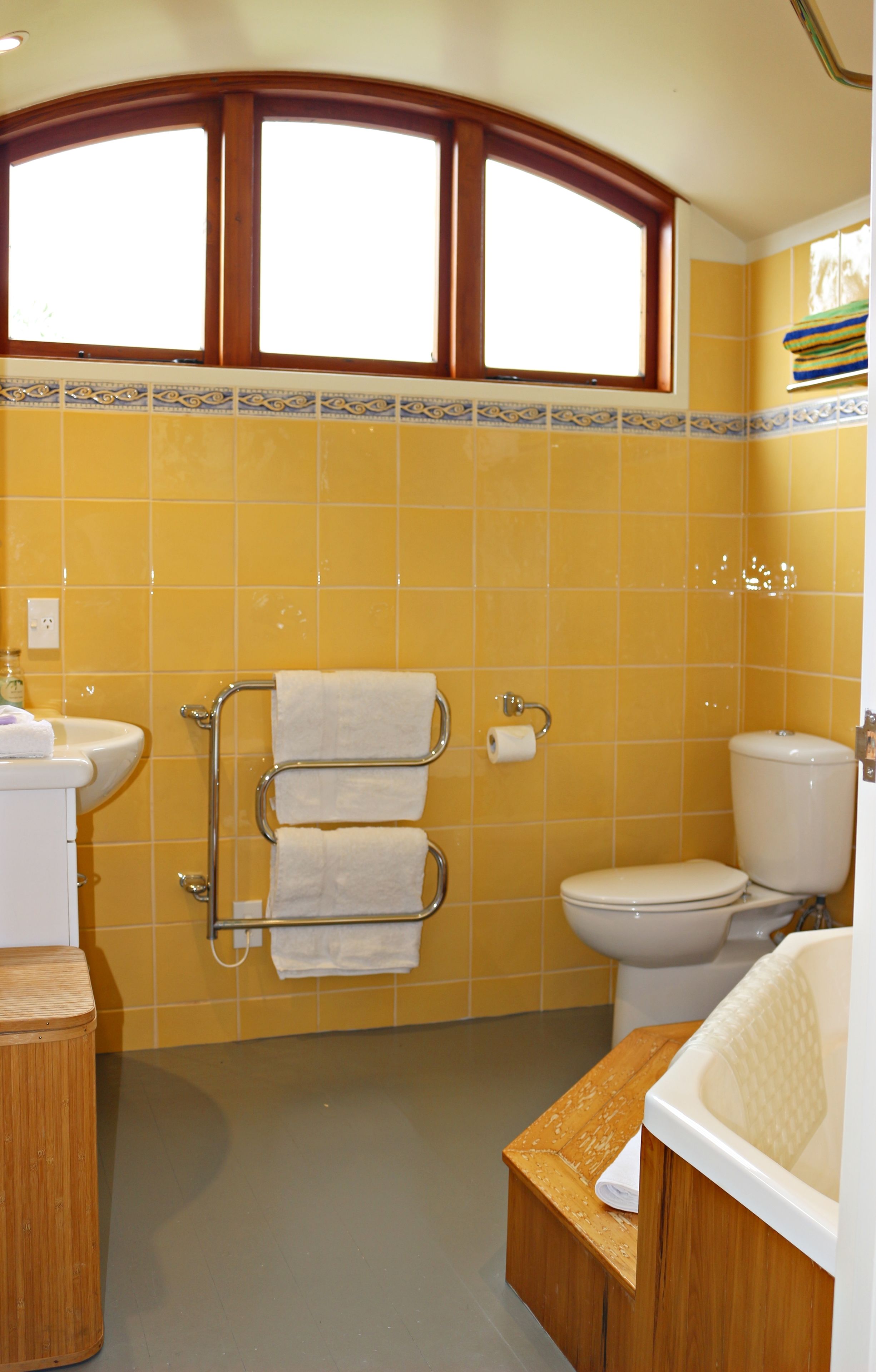 A bathroom with yellow tiles, a window above the sink, a toilet, and a bathtub.