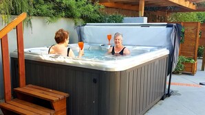 Ein Whirlpool mit zwei Personen, einer Holzterrasse und einem überdachten Bereich.