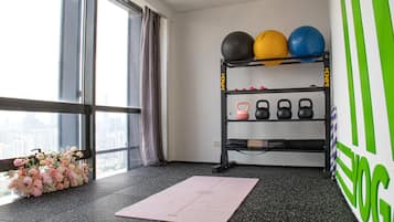 A room with a large window, a black exercise rack with weights, a pink yoga mat, and a floral arrangement.