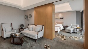 Habitación de hotel moderna con sofá, sillones, una mesa redonda de centro, una cama y una mesita auxiliar con fruta.