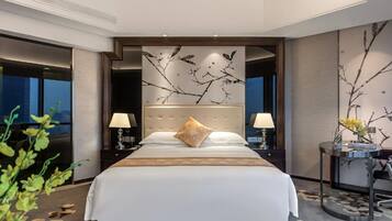 A hotel room with a large bed, two bedside tables with lamps, a decorative wall with a branch design, and a view of the city at night.