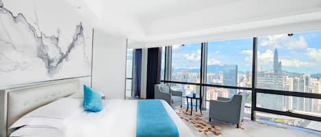 A modern hotel room with a large bed, a city view, and a balcony with seating.