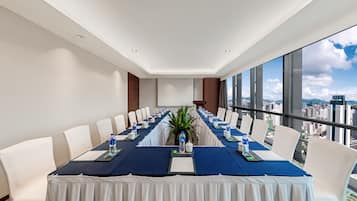 A conference room with a long table, white chairs, and a city view through large windows.