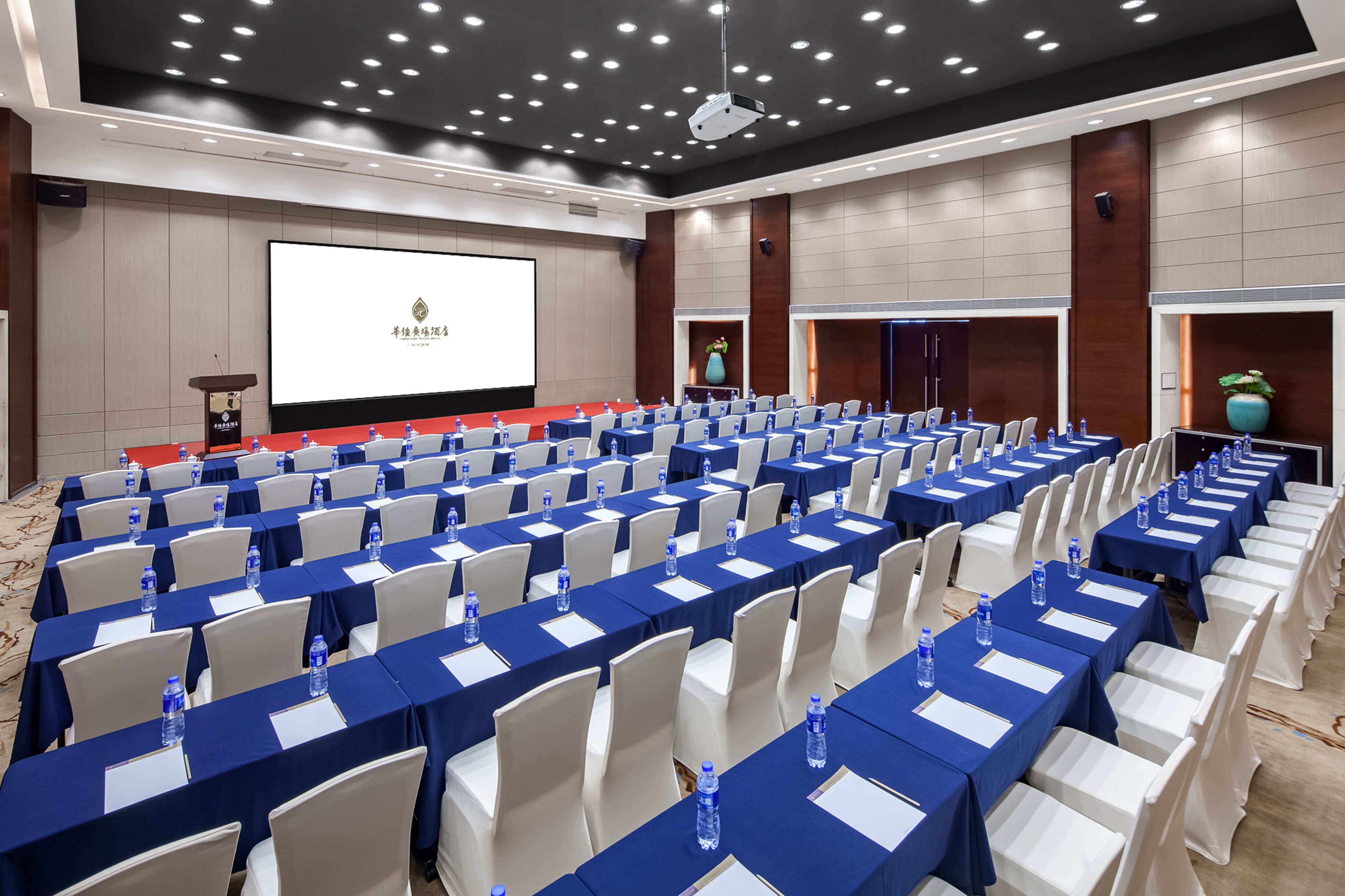Une salle de conférence avec des rangées de tables, des chaises et un grand écran.