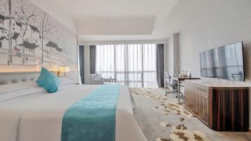 A hotel room with a large bed, a desk with a flat-screen TV, a view of the city through large windows, and a modern decor style.