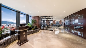 Un interior moderno con un mostrador de recepción de madera, una amplia estantería y vistas a la ciudad a través de grandes ventanales.