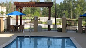 A rectangular pool with a metal ladder, surrounded by a fence and a pergola with blue umbrellas. - Hampton Inn & Suites Center (Center)