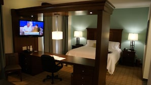 A hotel room with a desk, chair, television, two beds, nightstands, lamps, and a carpeted floor. - Hampton Inn & Suites Center (Center)