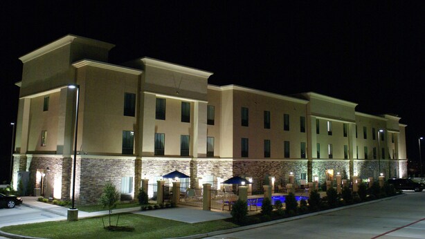 A multi-story hotel with a stone facade, outdoor seating area with umbrellas, and a swimming pool with blue lighting.