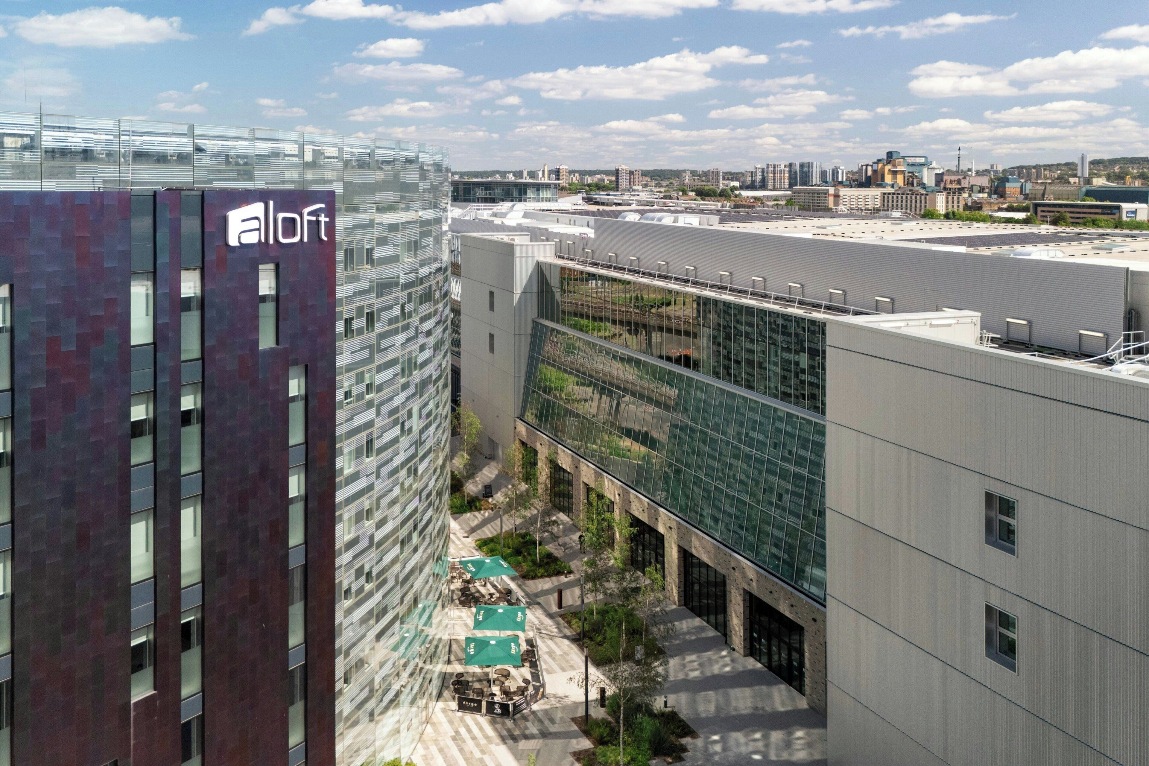A modern building with a glass facade, a rooftop terrace with outdoor seating, and a clear view of the city skyline.