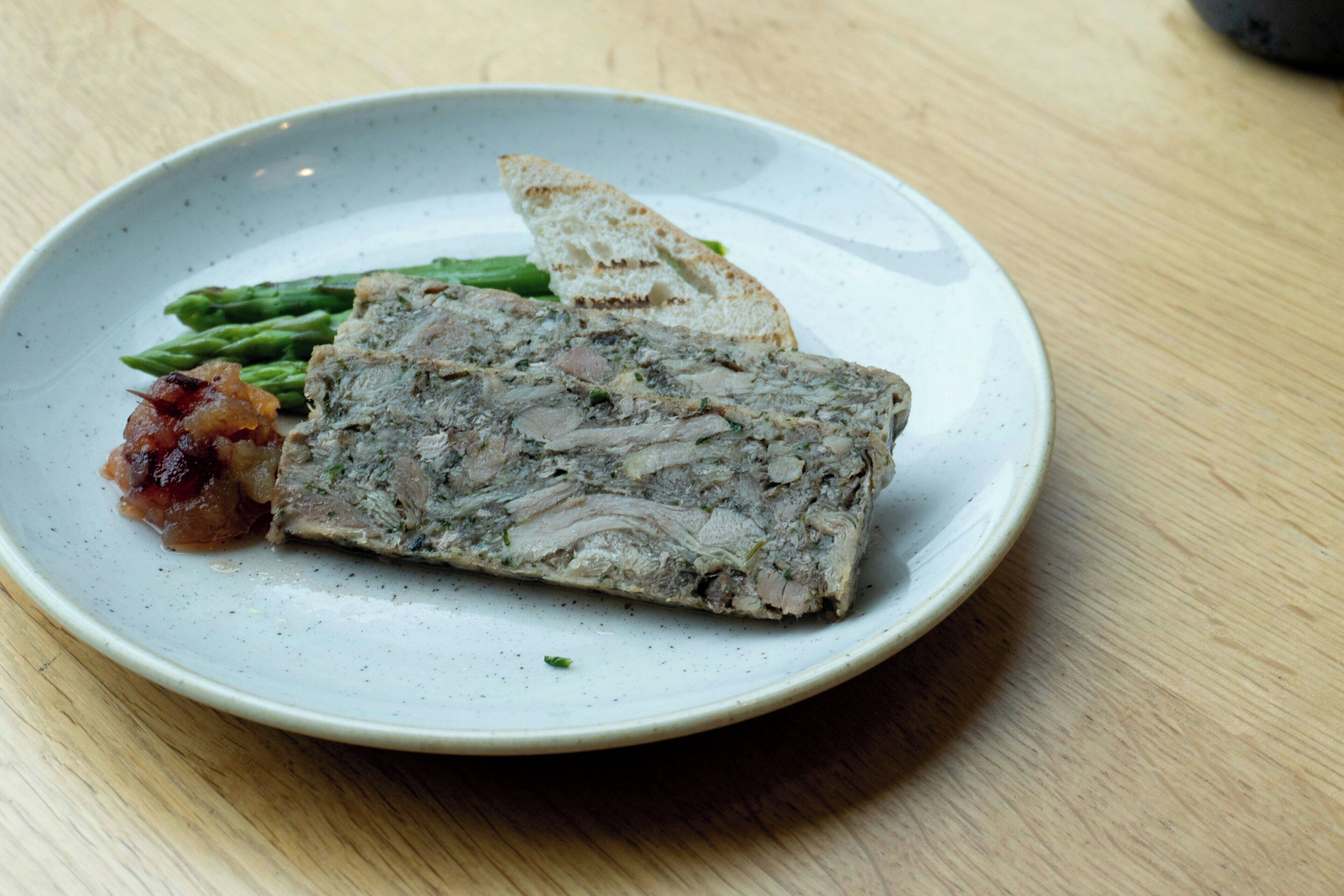 Un plato con un guiso de carne, espárragos y una rebanada de pan sobre una mesa.