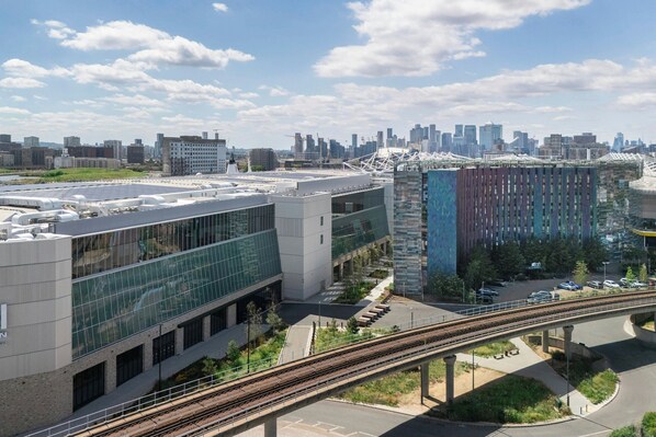 A modern building with a glass facade, a train track running alongside, and a city skyline in the background.