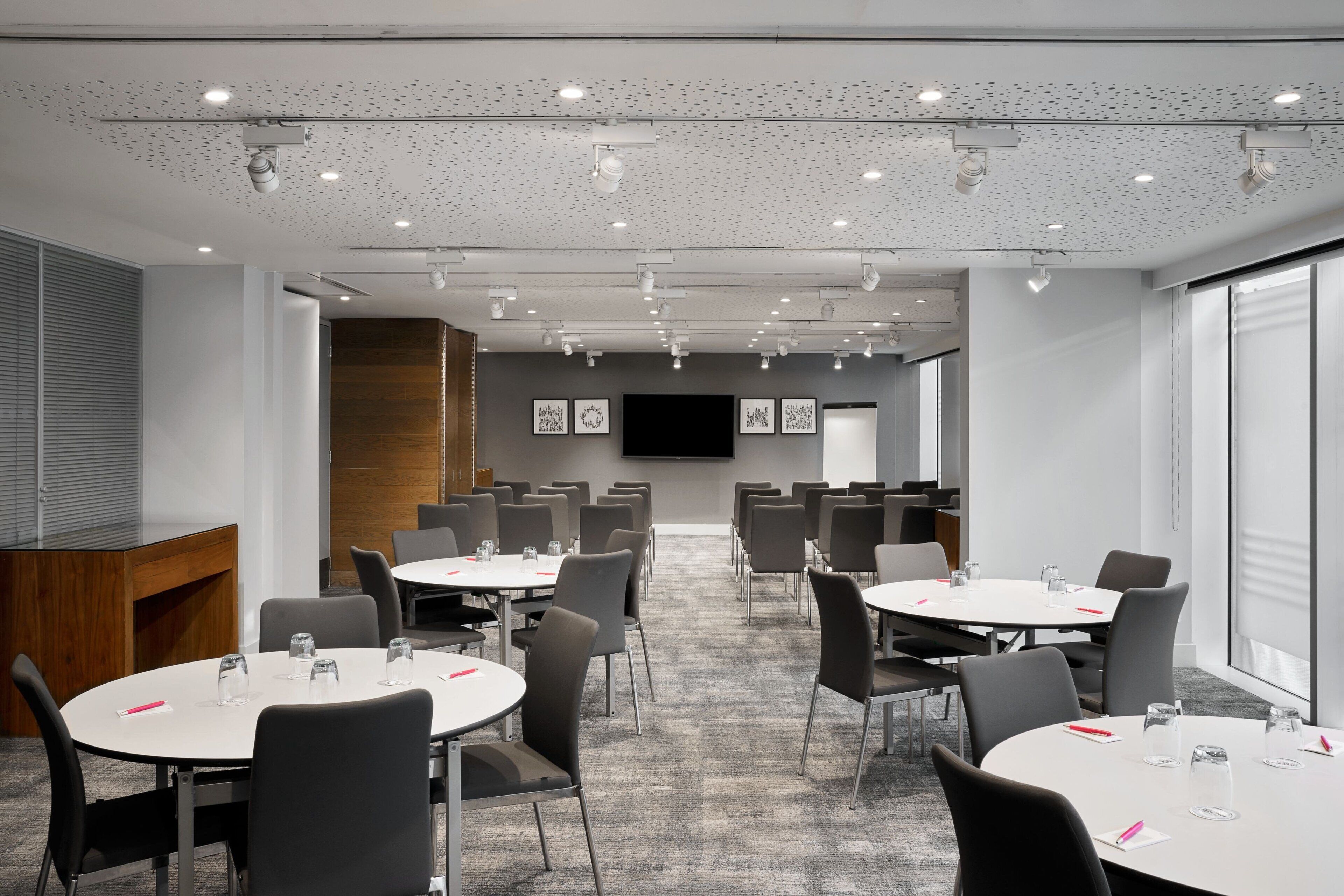 A conference room with round tables, chairs, and a large screen.
