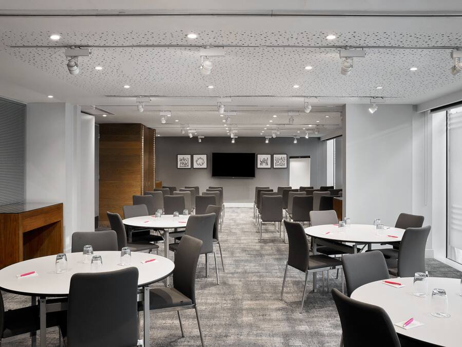 A conference room with round tables, chairs, and a large screen.
