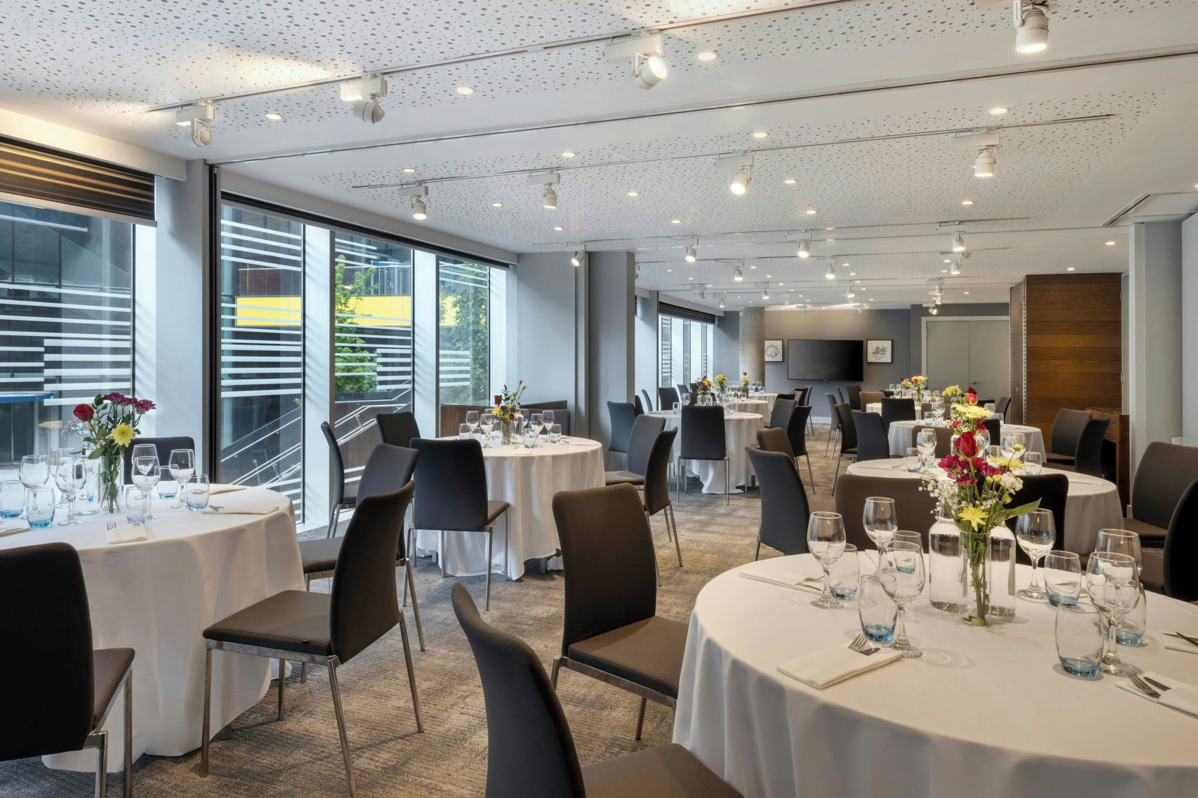 Una sala da pranzo moderna con tavoli rotondi, sedie e un'ampia finestra con tende.