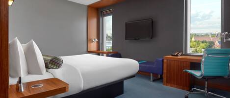 A modern hotel room with a bed, a desk, a chair, a TV, and a window with a city view.