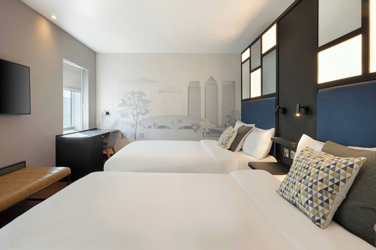 A hotel room with two beds, a desk, a chair, and a TV.