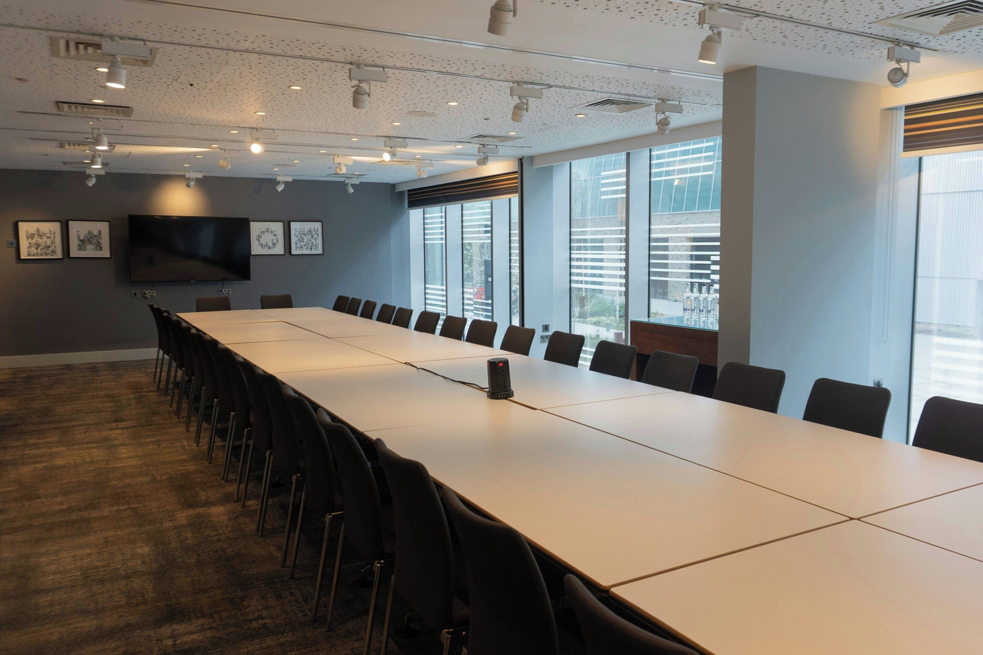 Une salle de conférence avec une longue table, des chaises, un projecteur et un téléviseur fixé au mur.