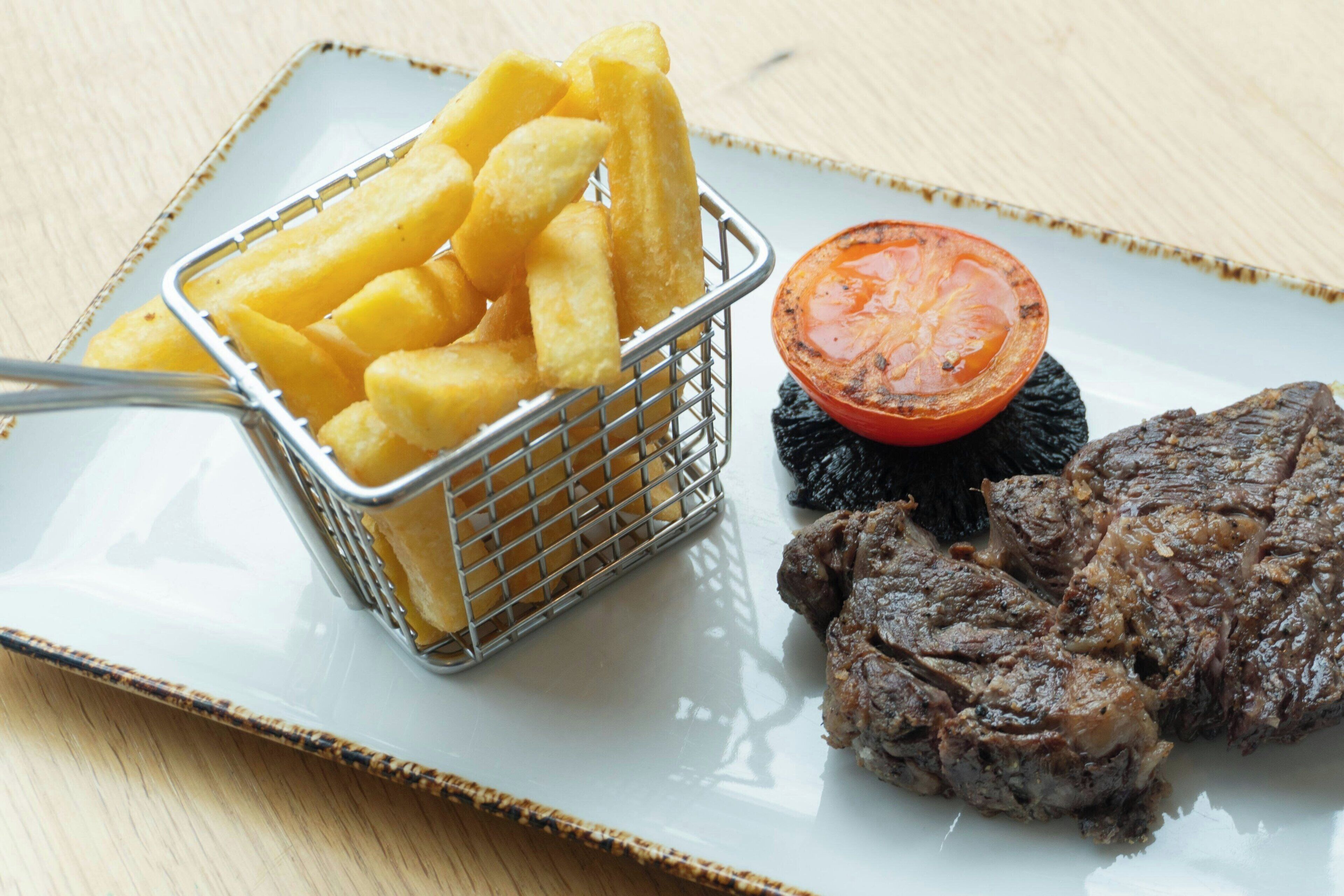 Un plato con un bistec, papas fritas y un tomate a la parrilla.