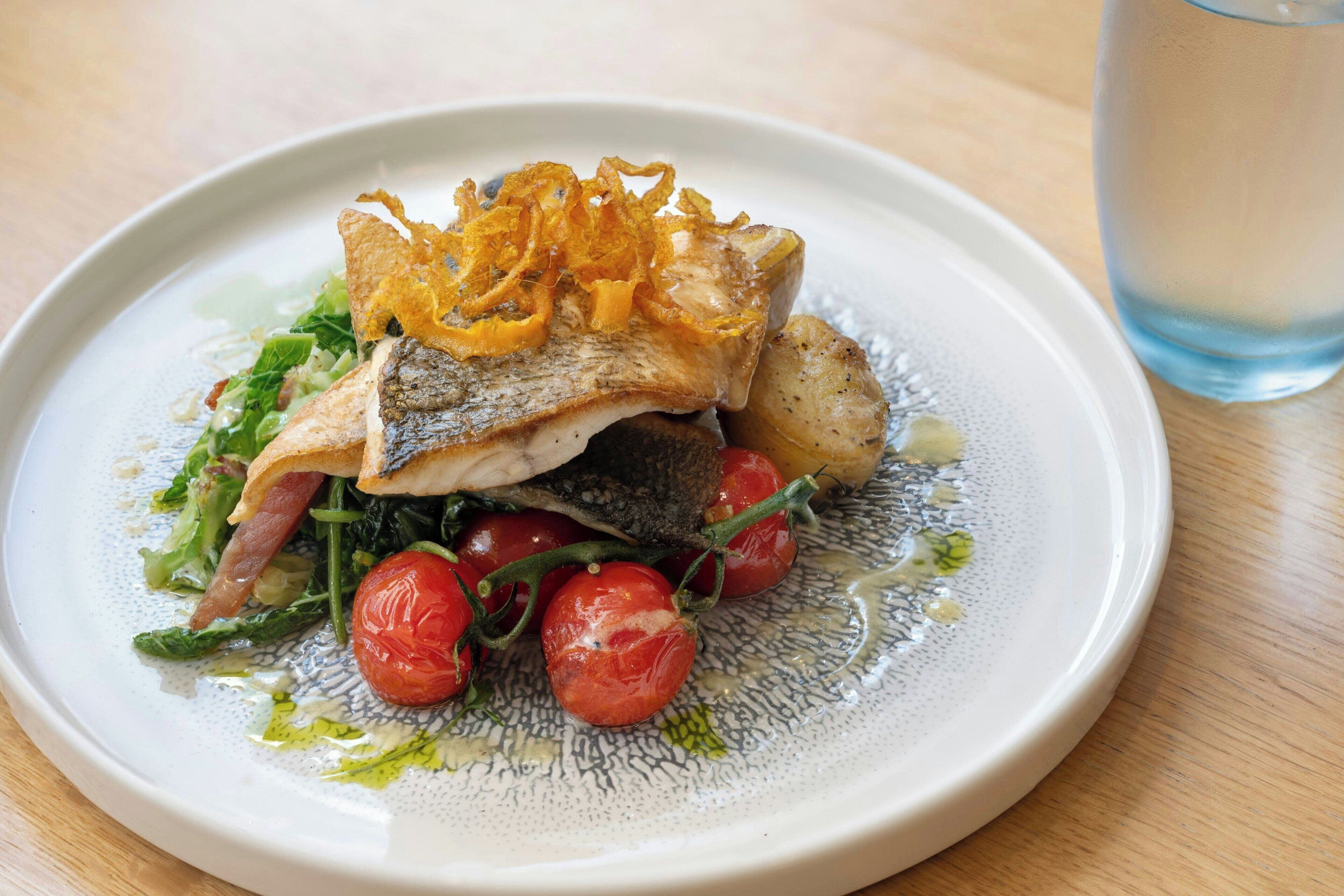 Ein Teller mit Fisch, Cocktailtomaten und knusprigem Garnitur.