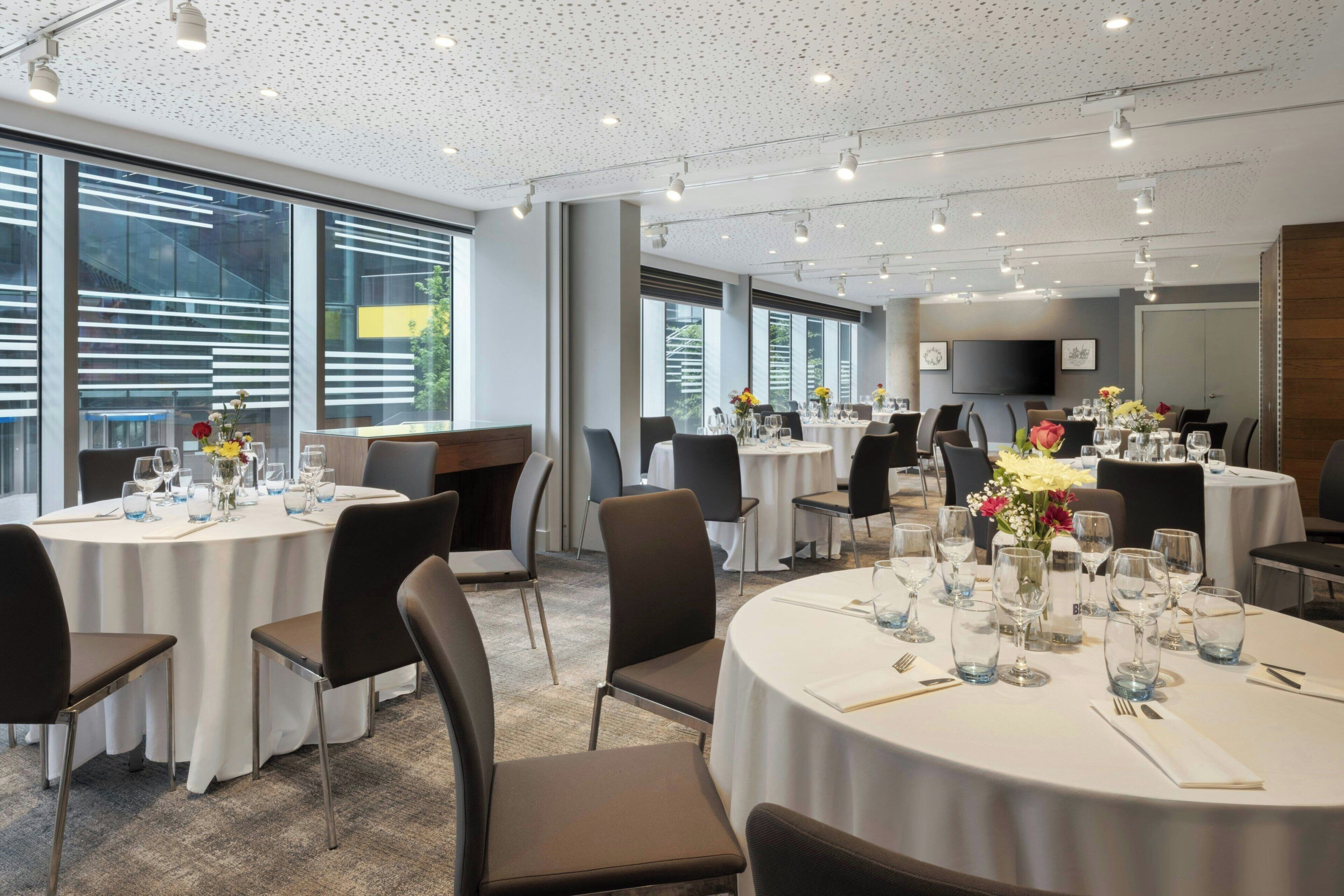 A modern dining area with round tables, chairs, and a ceiling with perforated panels.