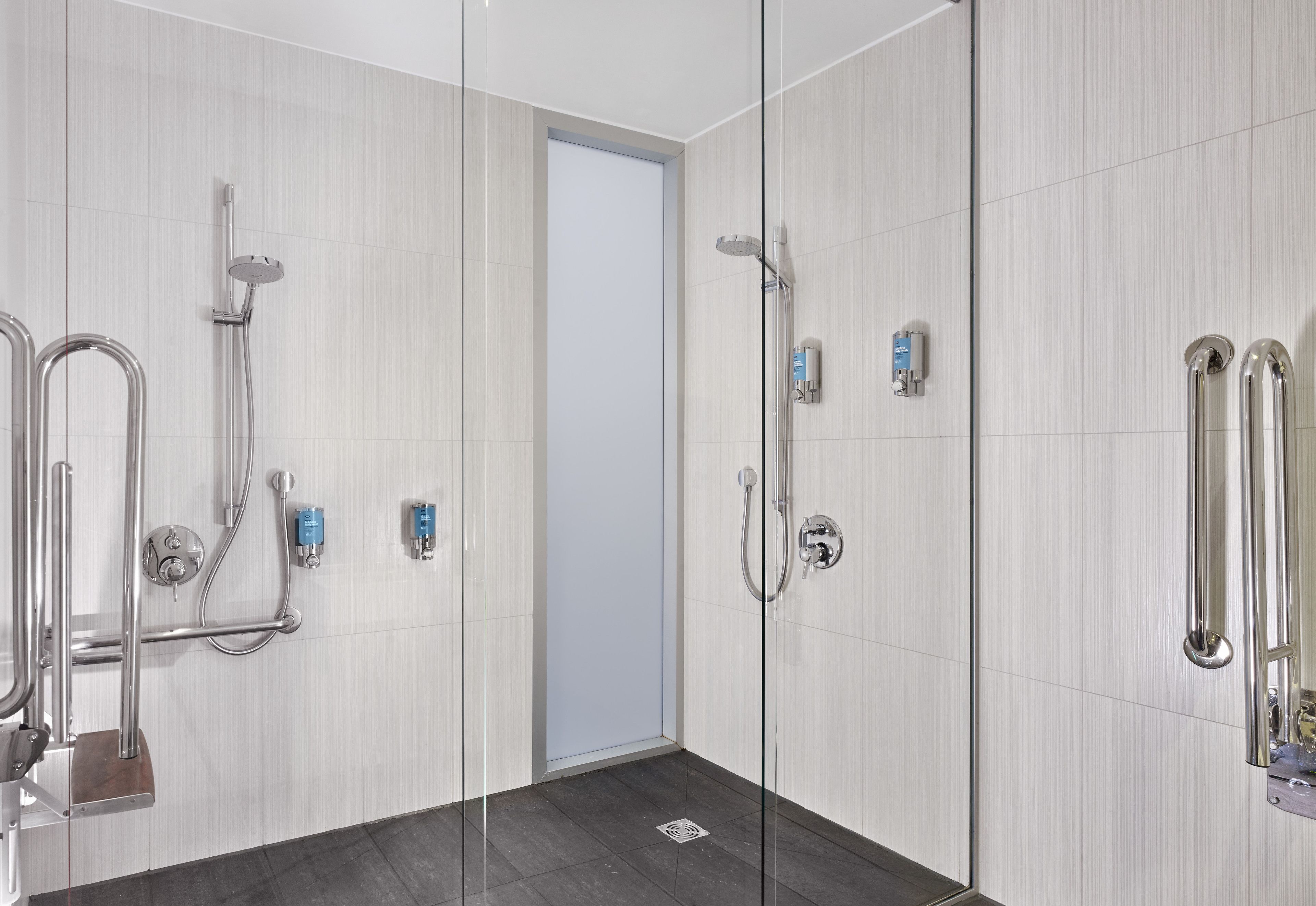 A modern shower area with glass doors, a handrail, and a showerhead.