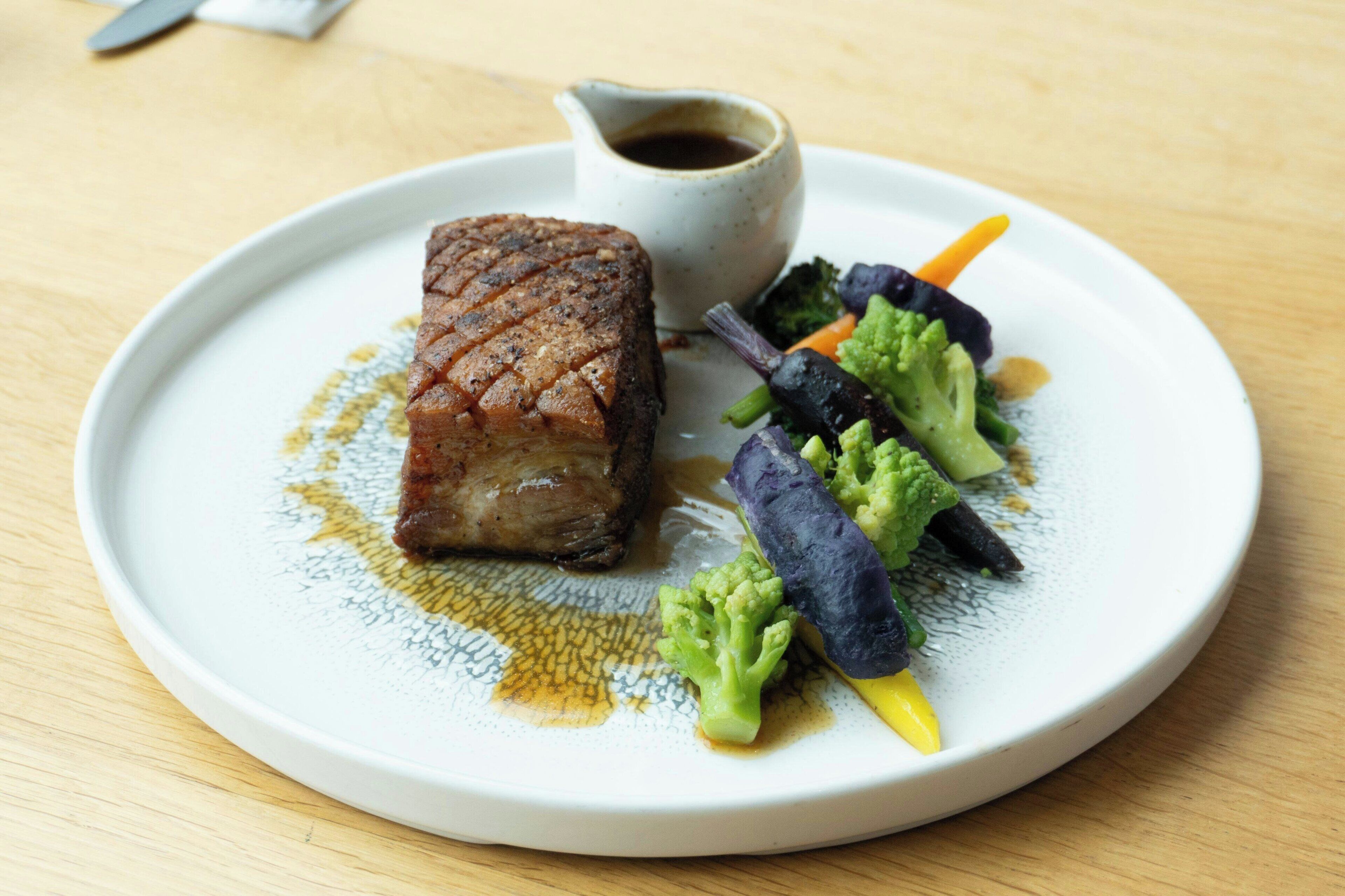 A plate with a piece of meat, vegetables, and a small sauce container.