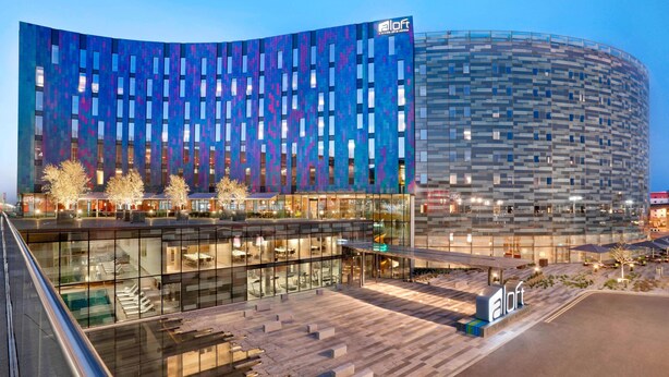 A modern hotel with a curved facade, large windows, and a spacious outdoor area with seating and a pool.