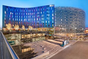 A modern hotel with a curved facade, large windows, and a spacious outdoor area with seating and a pool.