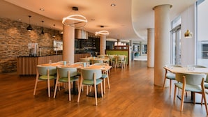 A modern dining area with wooden flooring, green upholstered chairs, and pendant lighting.