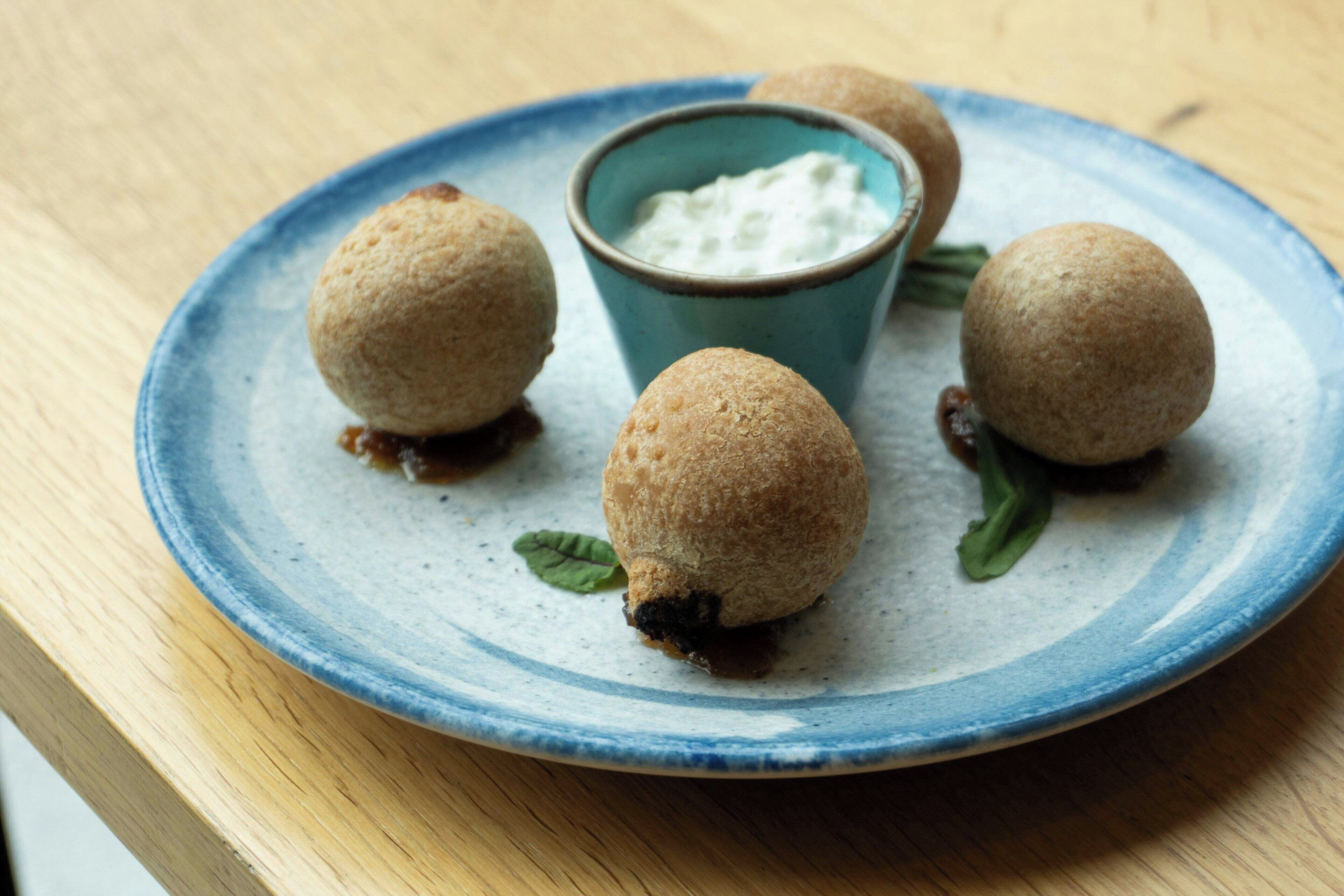 A plate with three round, golden-brown items and a small blue cup with a white creamy substance.