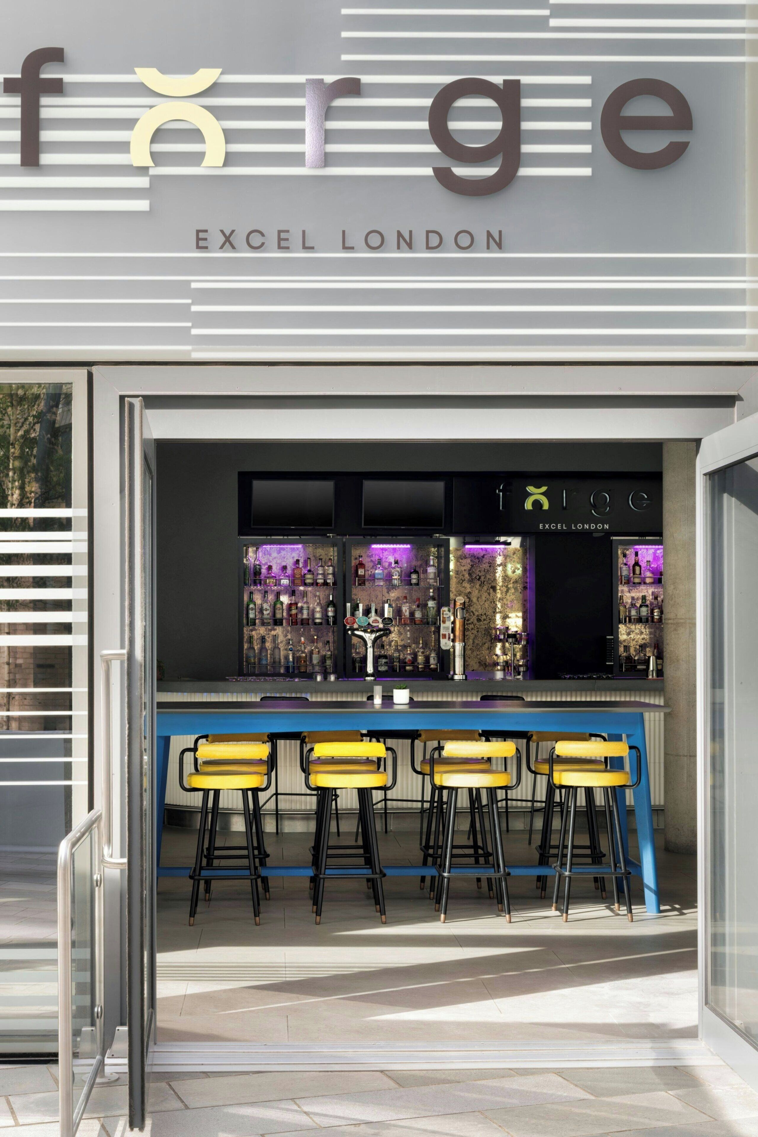 Um bar com banquetas e balcão, com a inscrição 'EXCEL LONDON' acima.
