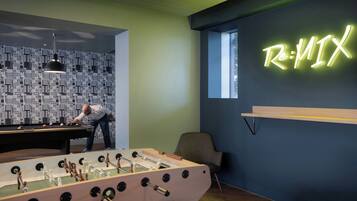 Ein Zimmer mit einem Kicker, einer Neon-Schriftzugtafel mit der Aufschrift "Re:MIX" und einer Wand mit strukturiertem Wandpapier.