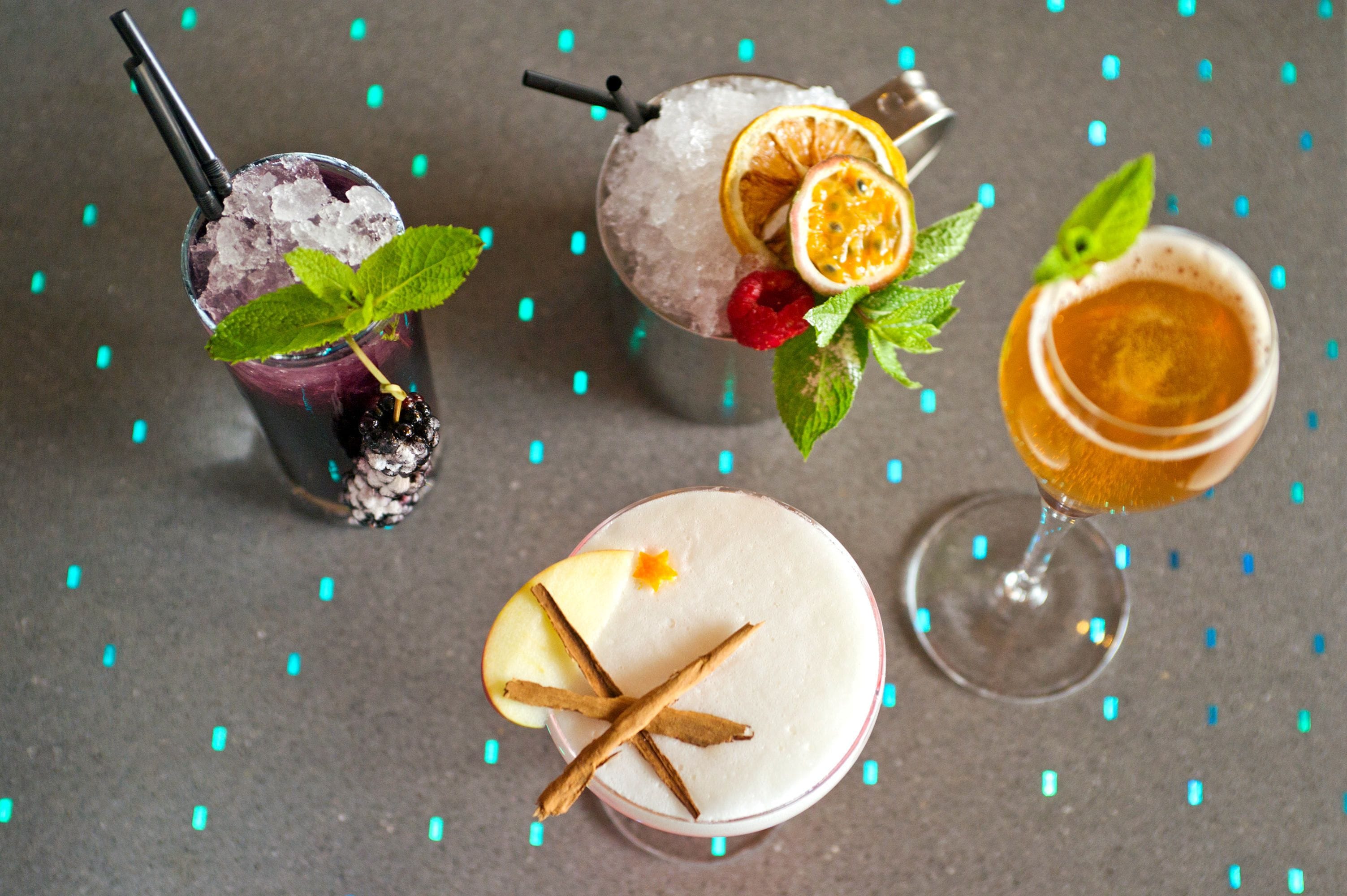 Three cocktails with garnishes and ice, on a table with a grey surface and blue decorative elements.