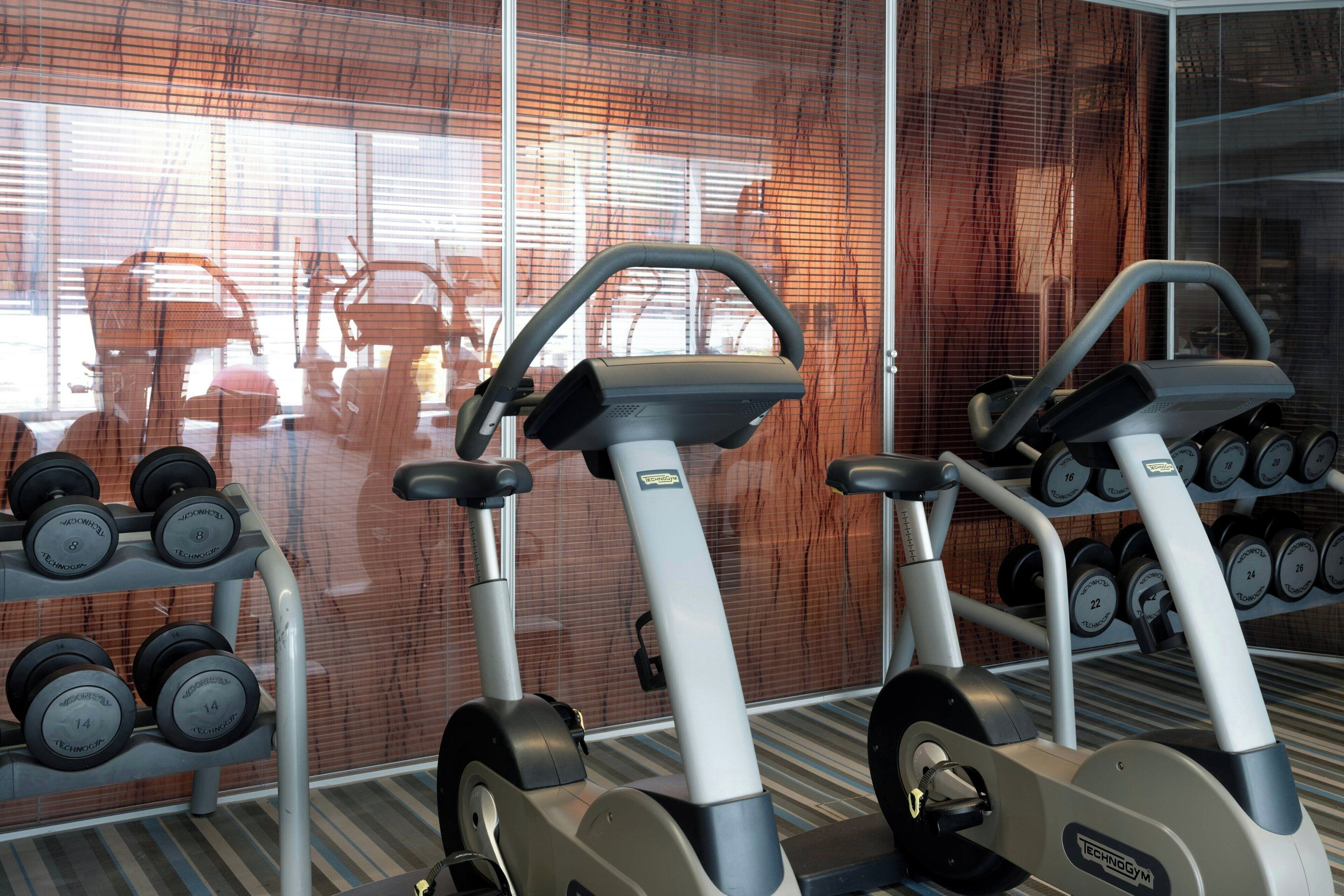 A gym with cardio machines, dumbbells, and a mirrored wall reflecting exercise equipment.